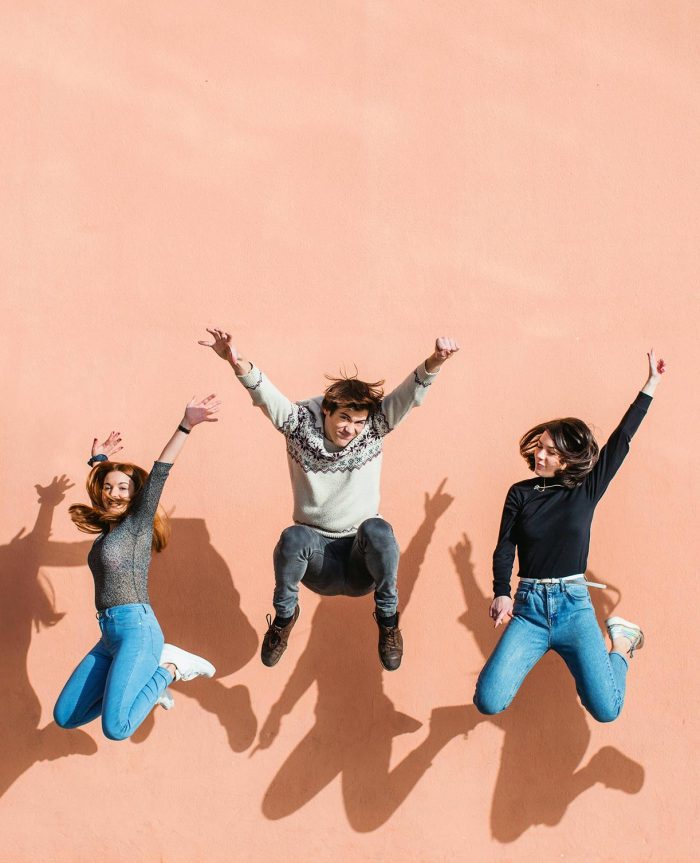 Photo of three people jumping infront of pink wall